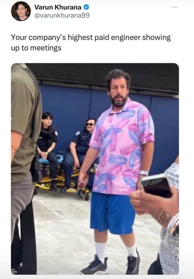 A tweet from Varun Khurana reading “Your company's highest paid engineer showing up to meetings,” above a paparazzi photo of Adam Sandler in a loose floral polo shirt, blue gym shorts, and sneakers, walking past a group of uniformed staff.